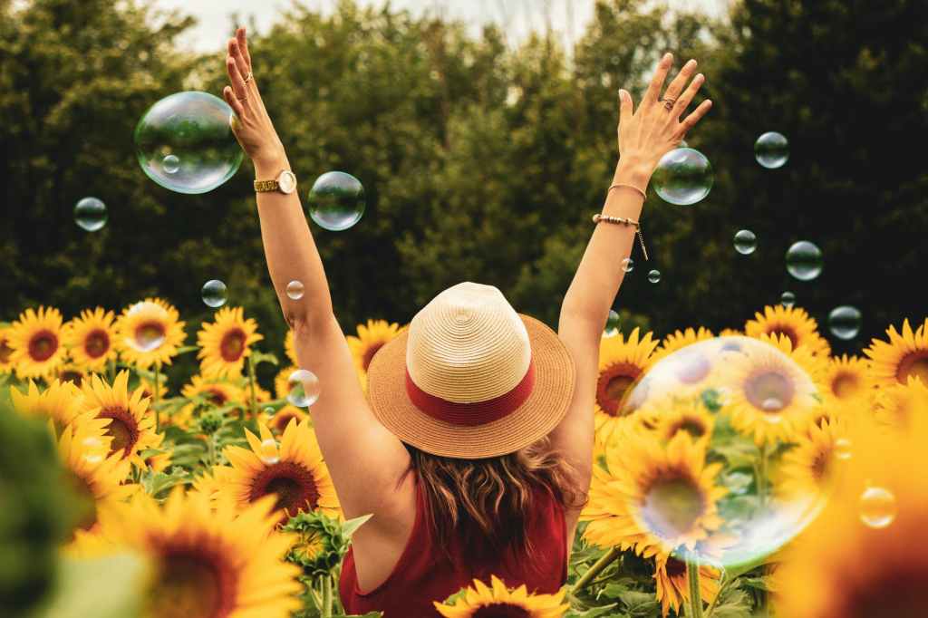 White lady raising her hands in the air in a sunflower field with bubbles 