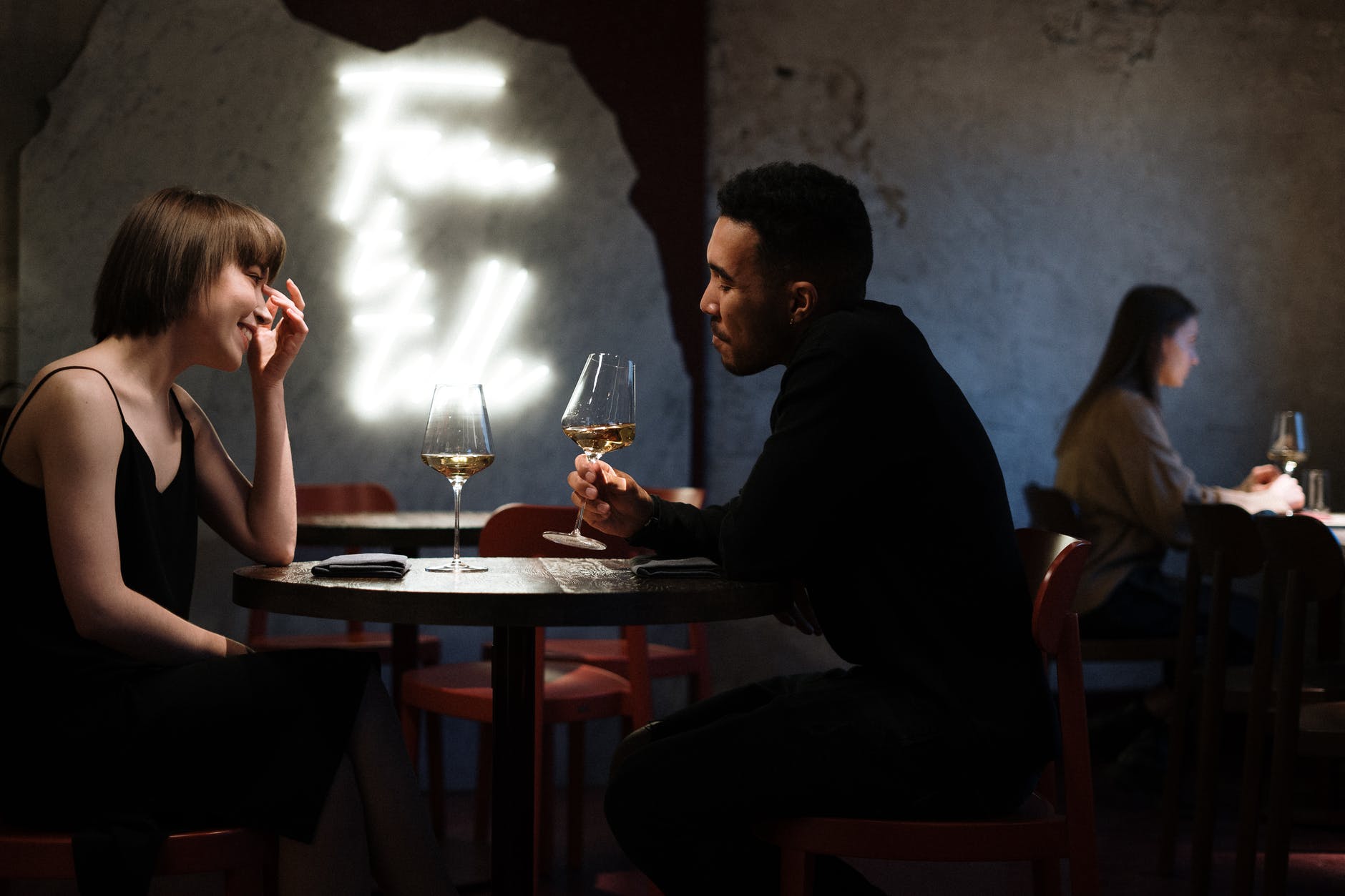 Interracial couple paired by high end professional matchmakers for elite singles on a dinner date drinking wine at a table