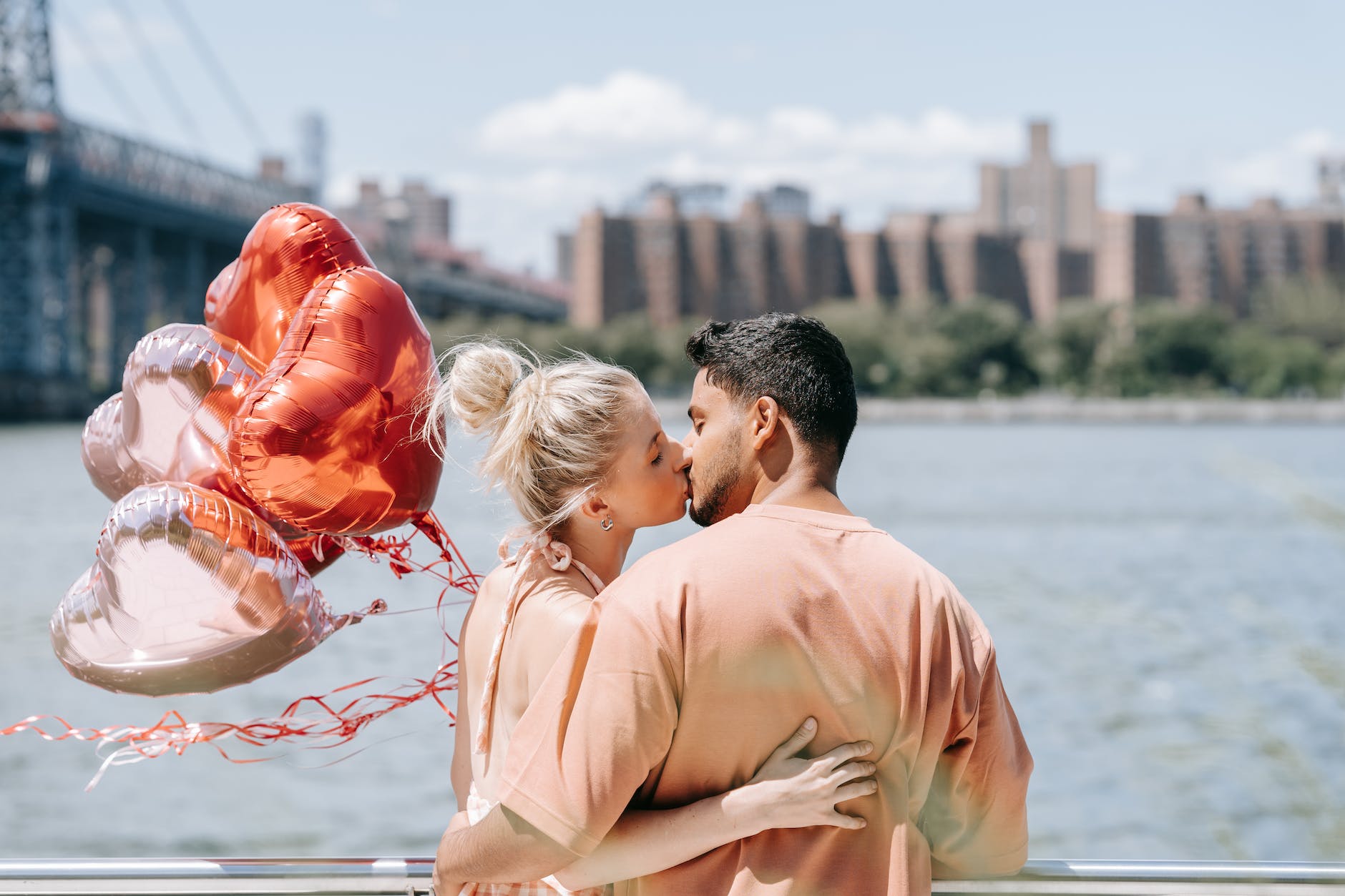 Caucasian couple kissing by a river holding balloons
