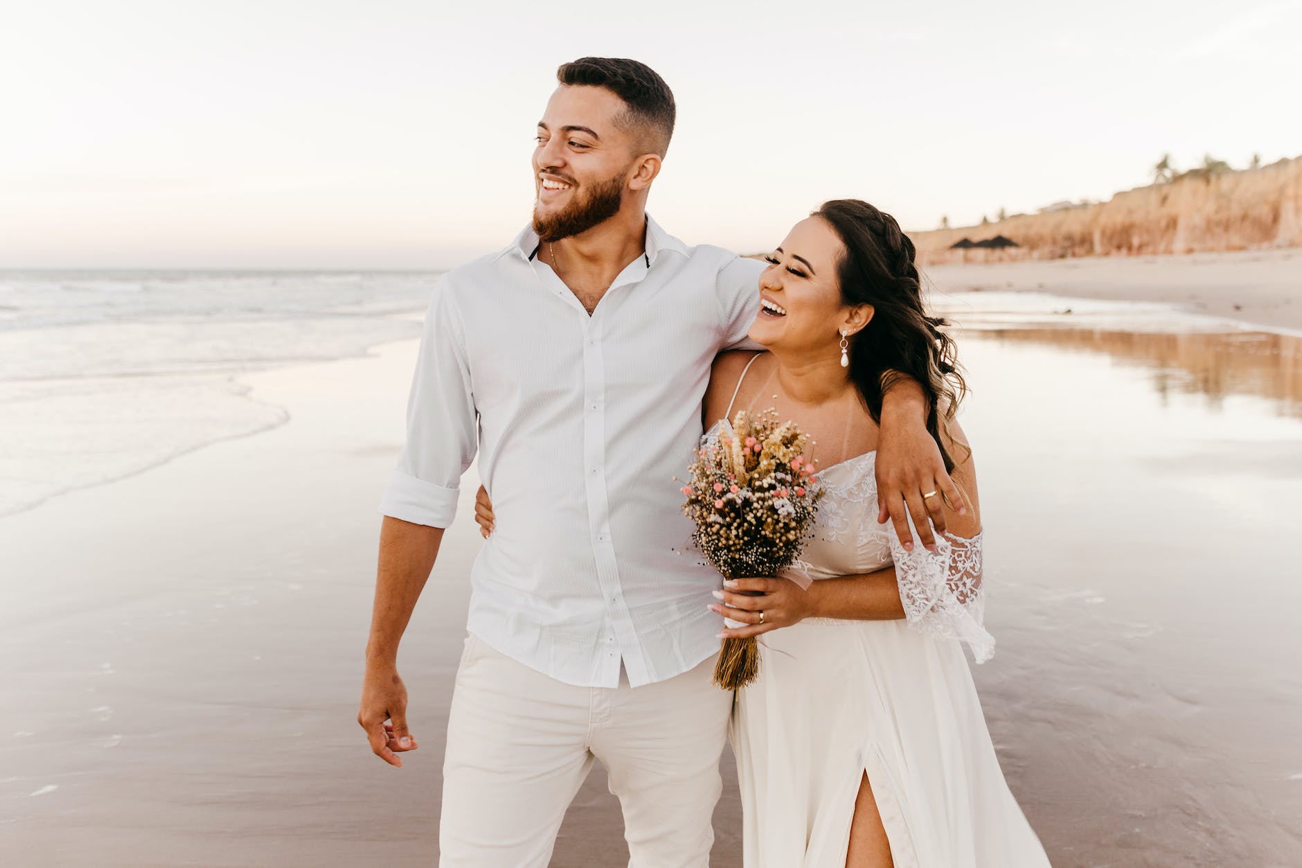 Newlywed Hispanic couple paired by matchmakers in Los Angeles embracing and walking on a beach