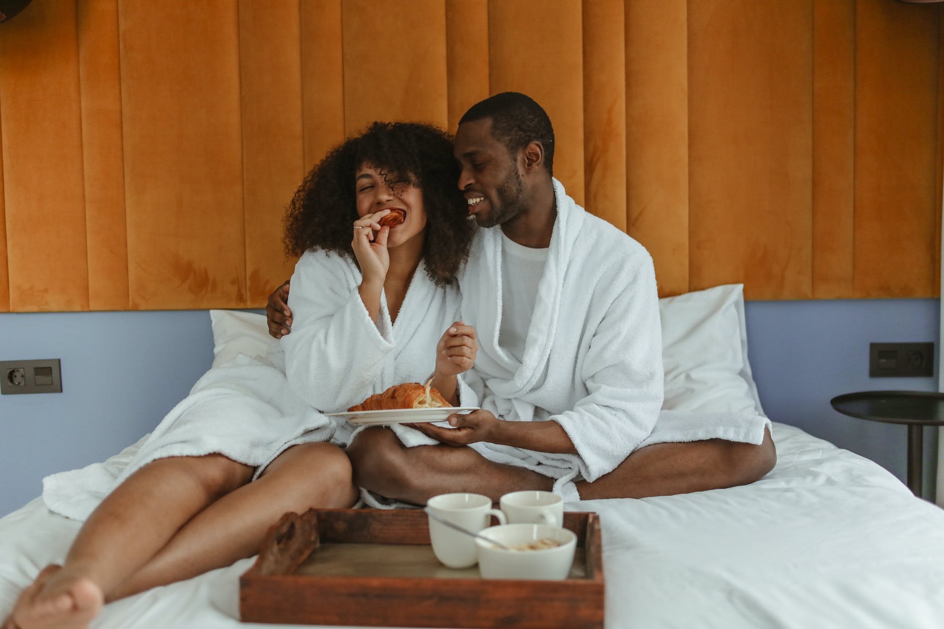 Black couple in white robes cuddling on a bed