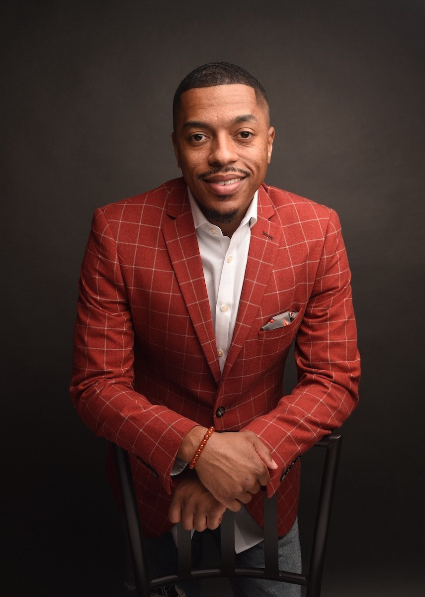 Dating coach for men Michael Smoke wearing a red suit and smiling while leaning on a chair