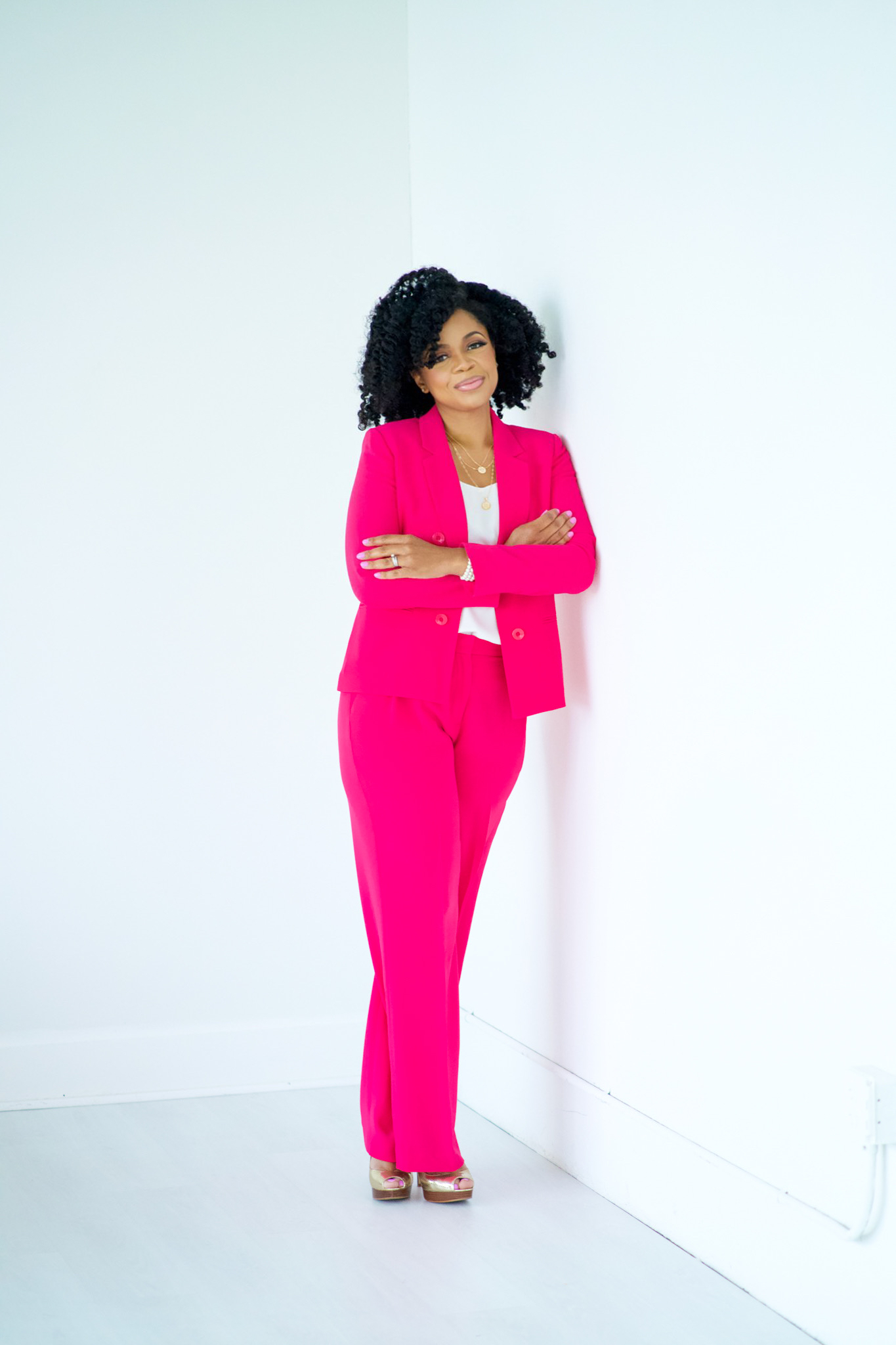 Black matchmaker Lauren Sanders in a pink suit while smiling and leaning on a white wall