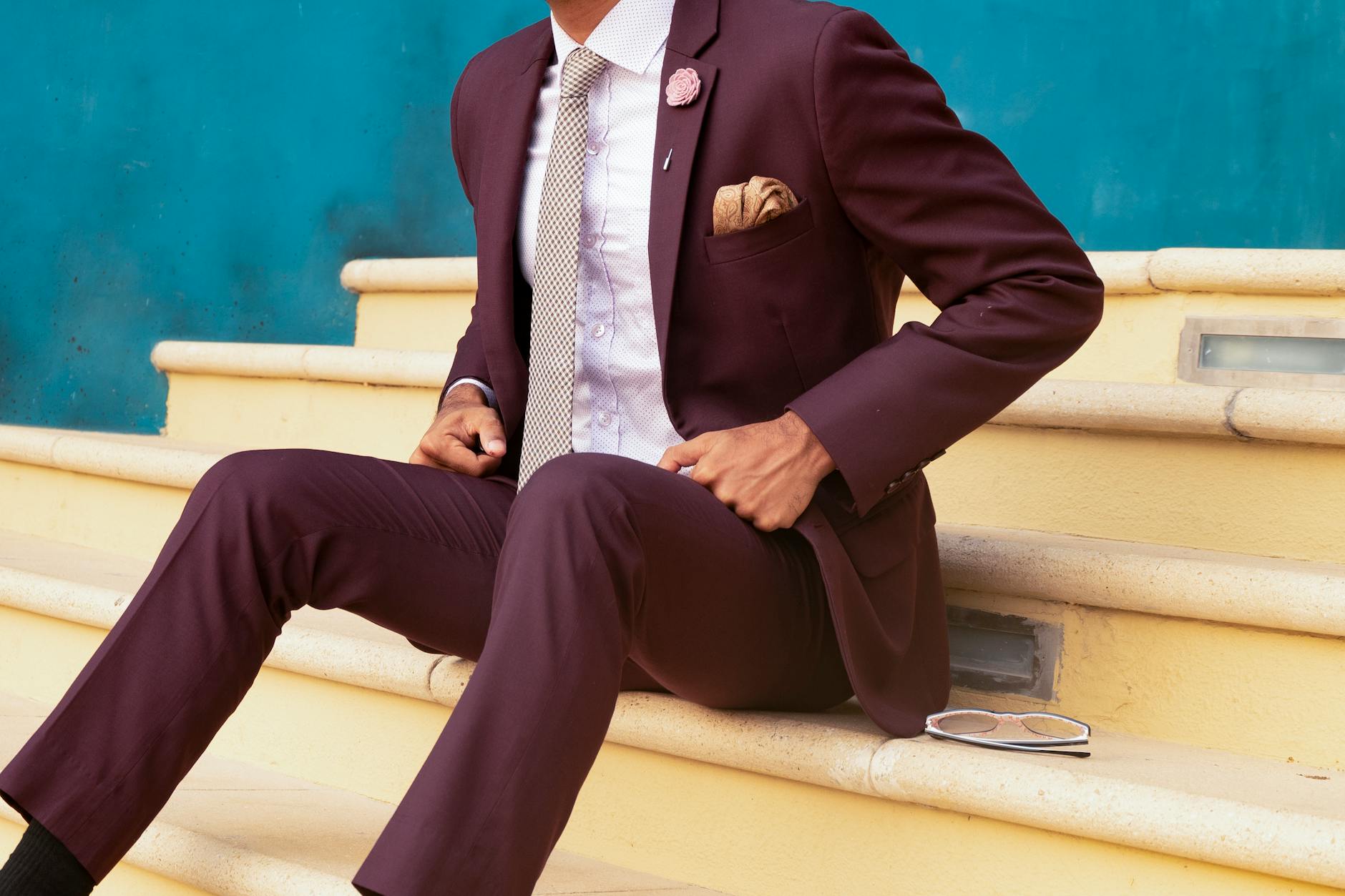 Dating coach for men sitting on cream stairs wearing a burgundy suit
