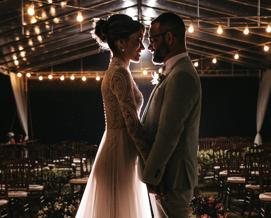 Caucasian couple standing up smiling at each other and holding hands on their wedding day
