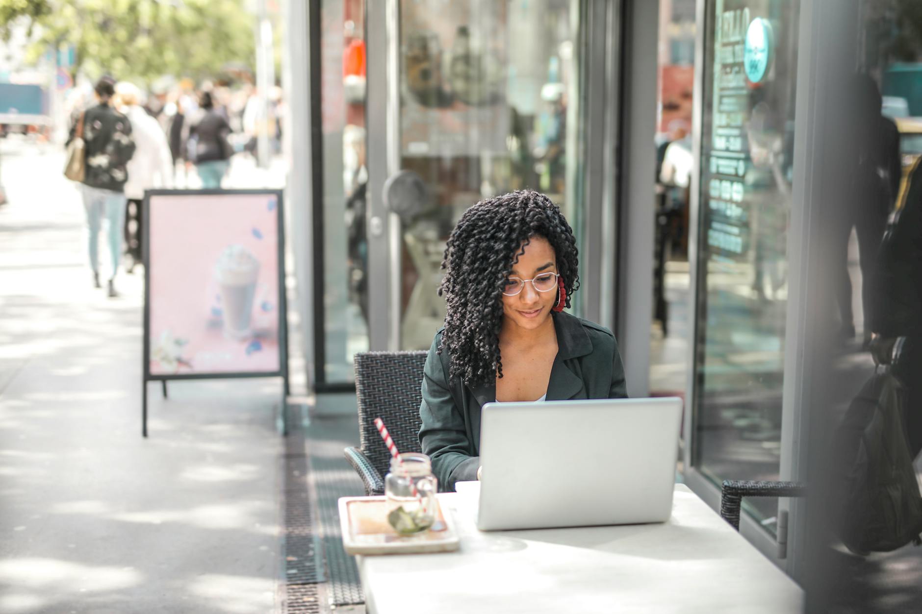 A black matchmaker near me sitting at a table outside of a restaurant on her computer