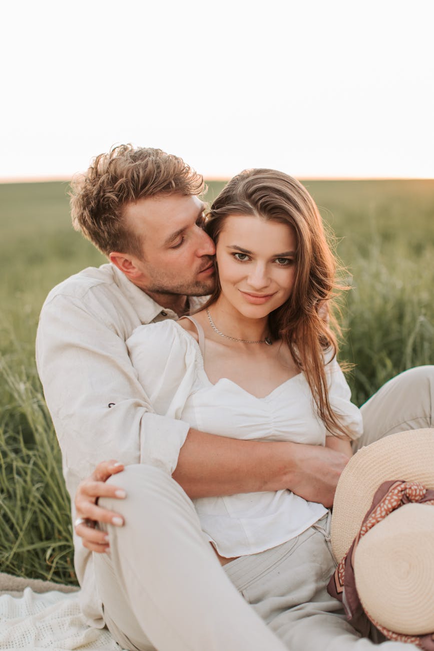 Caucasian couple kissing in the grass while woman stares at the camera
