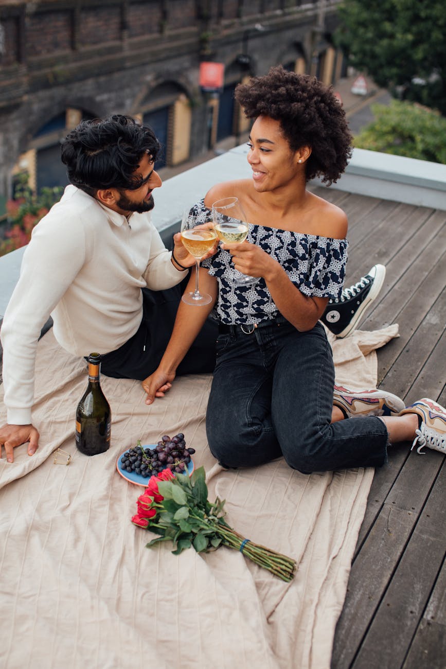 Interracial couple on a date sitting on a rooftop in the city with two glasses of wine