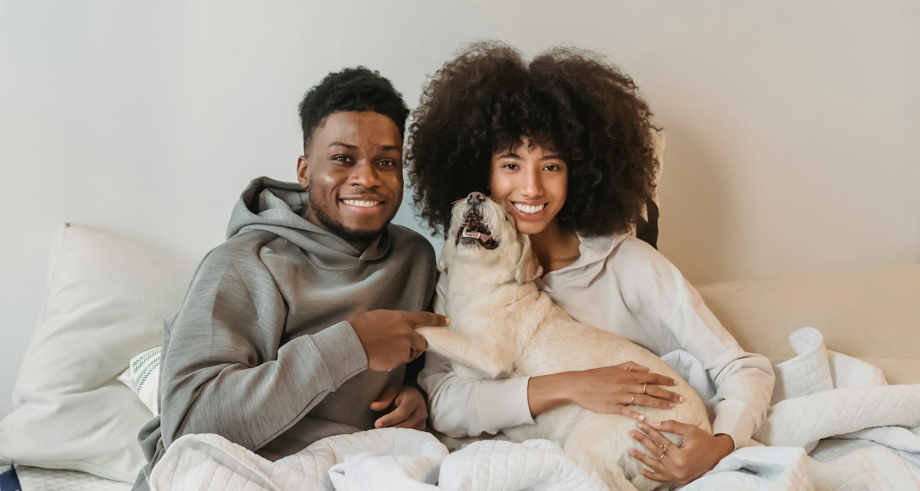Black couple introduced by matchmakers in Philadelphia sitting in bed while holding cute dog
