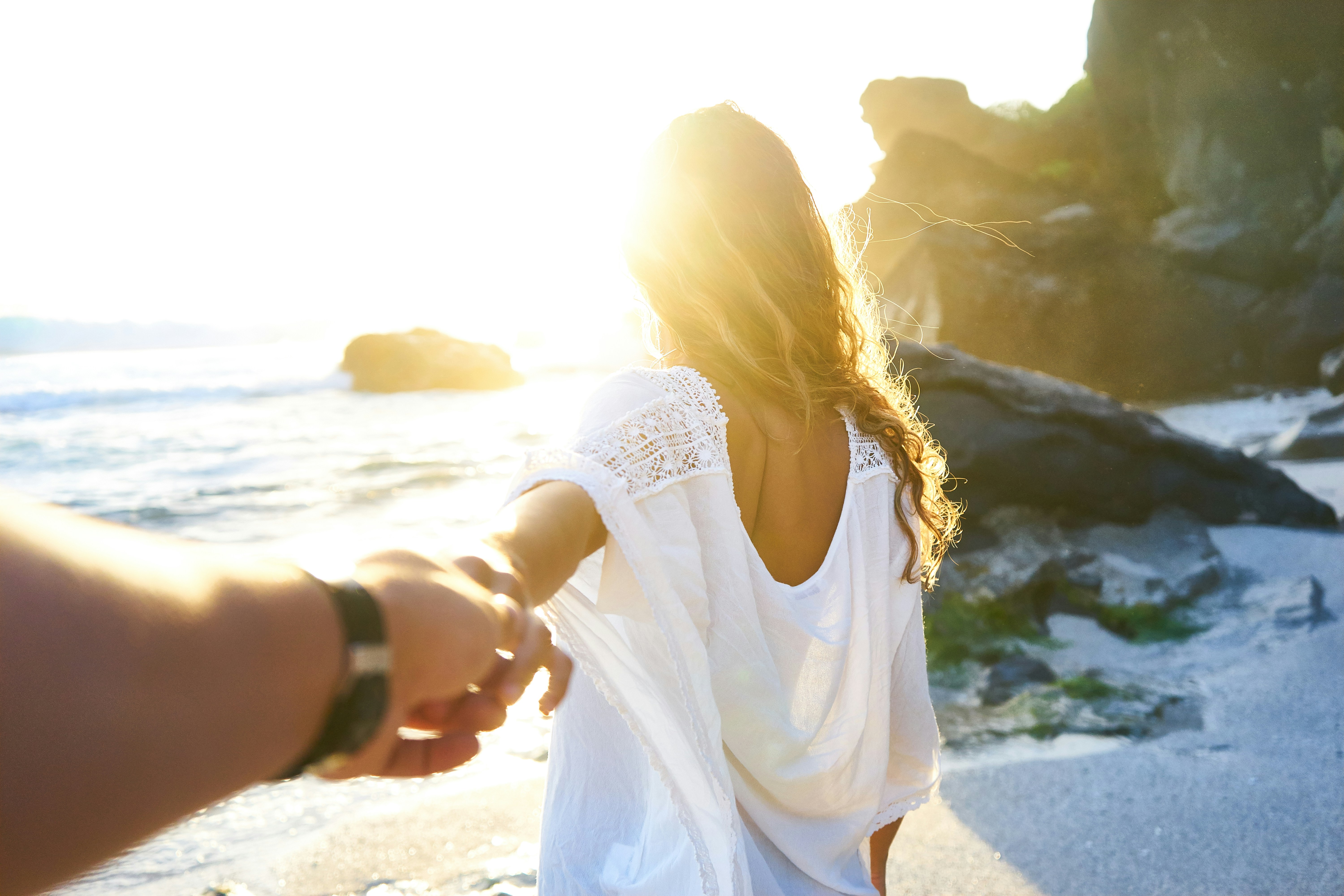 White couple paired by Fort Lauderdale matchmakers holding hands by rocks on a beach