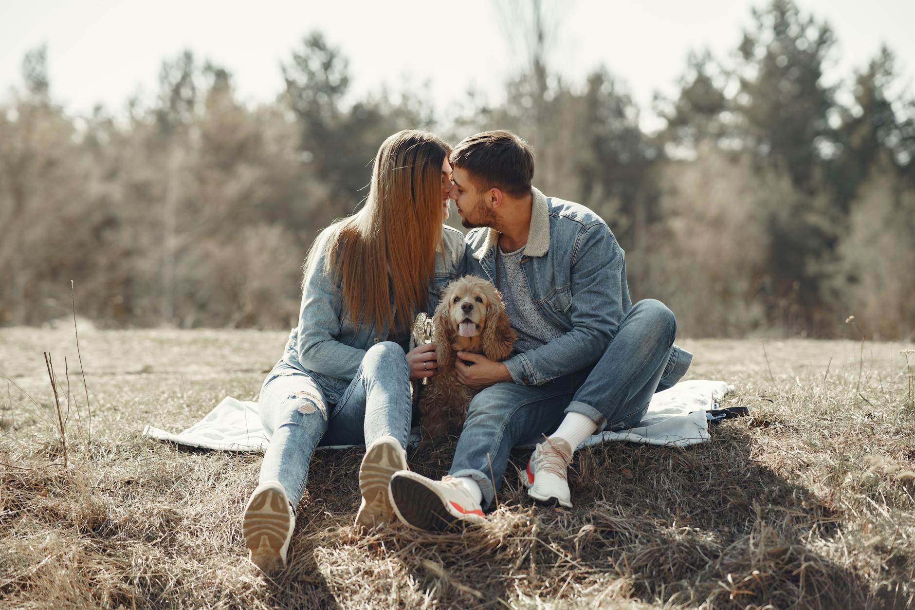 White couple cuddling while holding a cute dog on a blanket in the grass