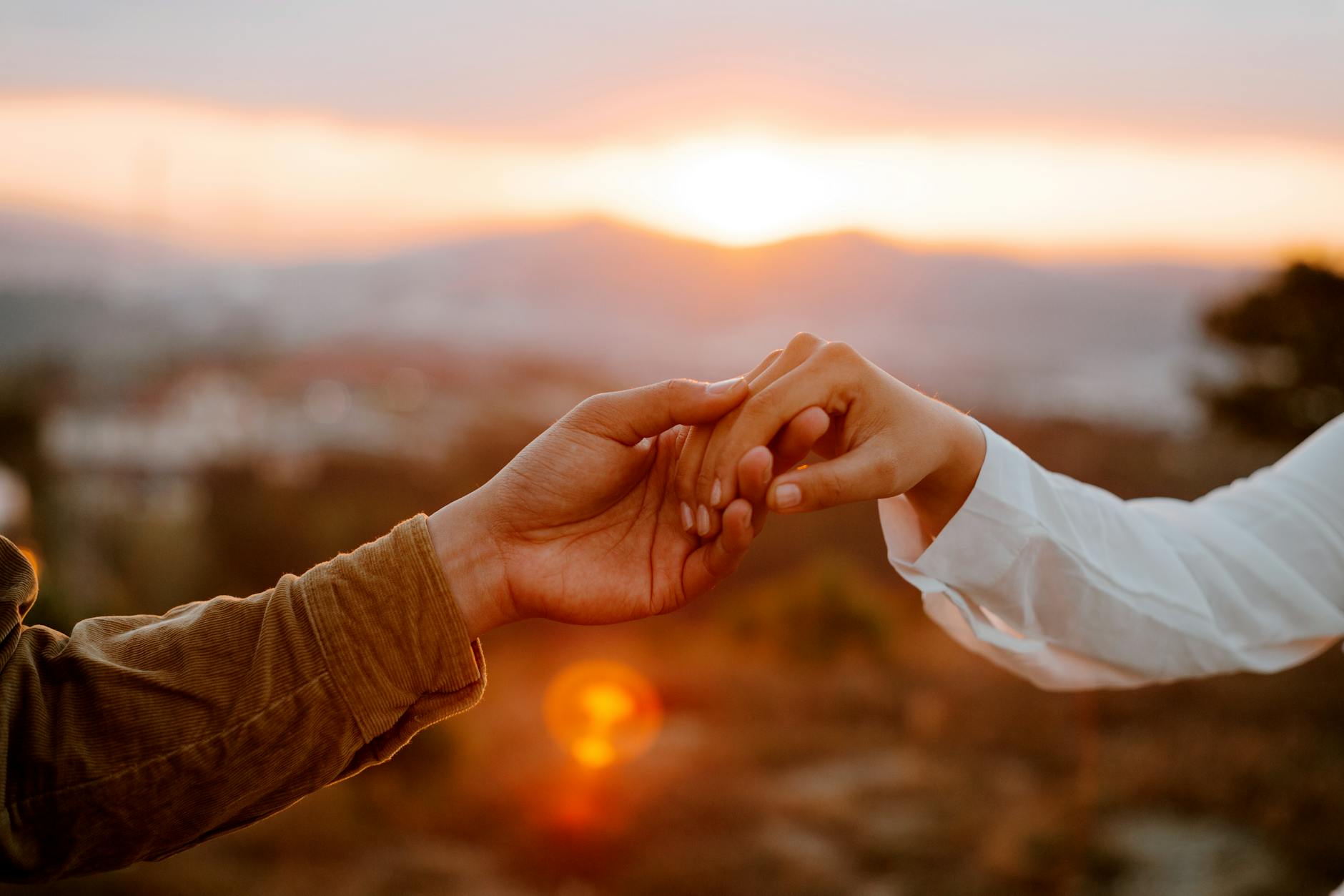 Couple holding hands at sunset with a view of mountains in the background
