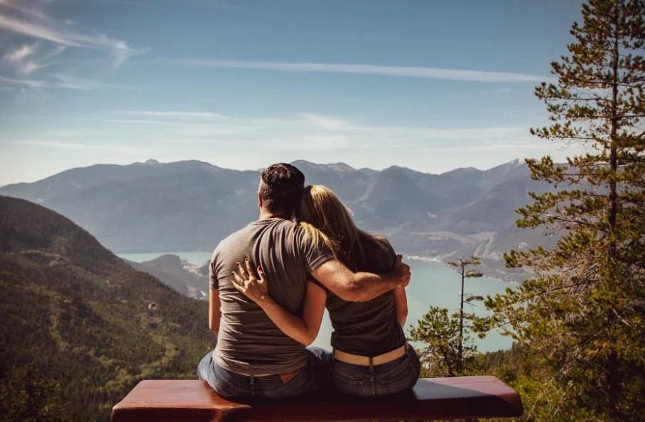 Cute Caucasian couple paired by matchmakers in Denver sitting in the mountains looking at a lake