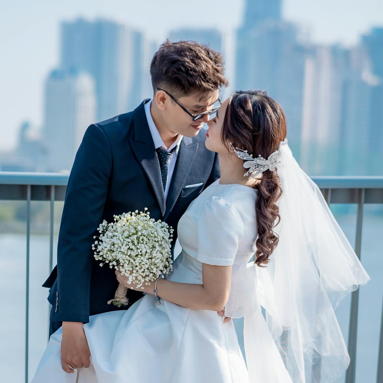 Newlywed Asian couple matched by dating coaches for women on their wedding day embracing for a picture with cityscape in the background
