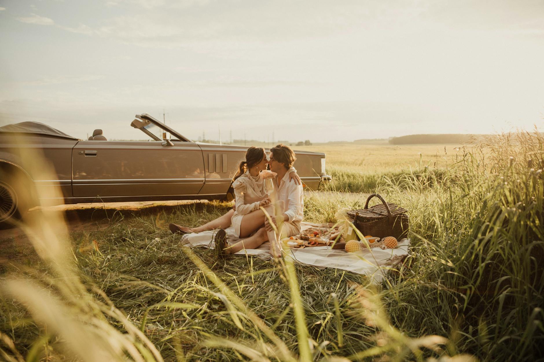 White couple paired by dating coaches kissing in a grassy field near a car