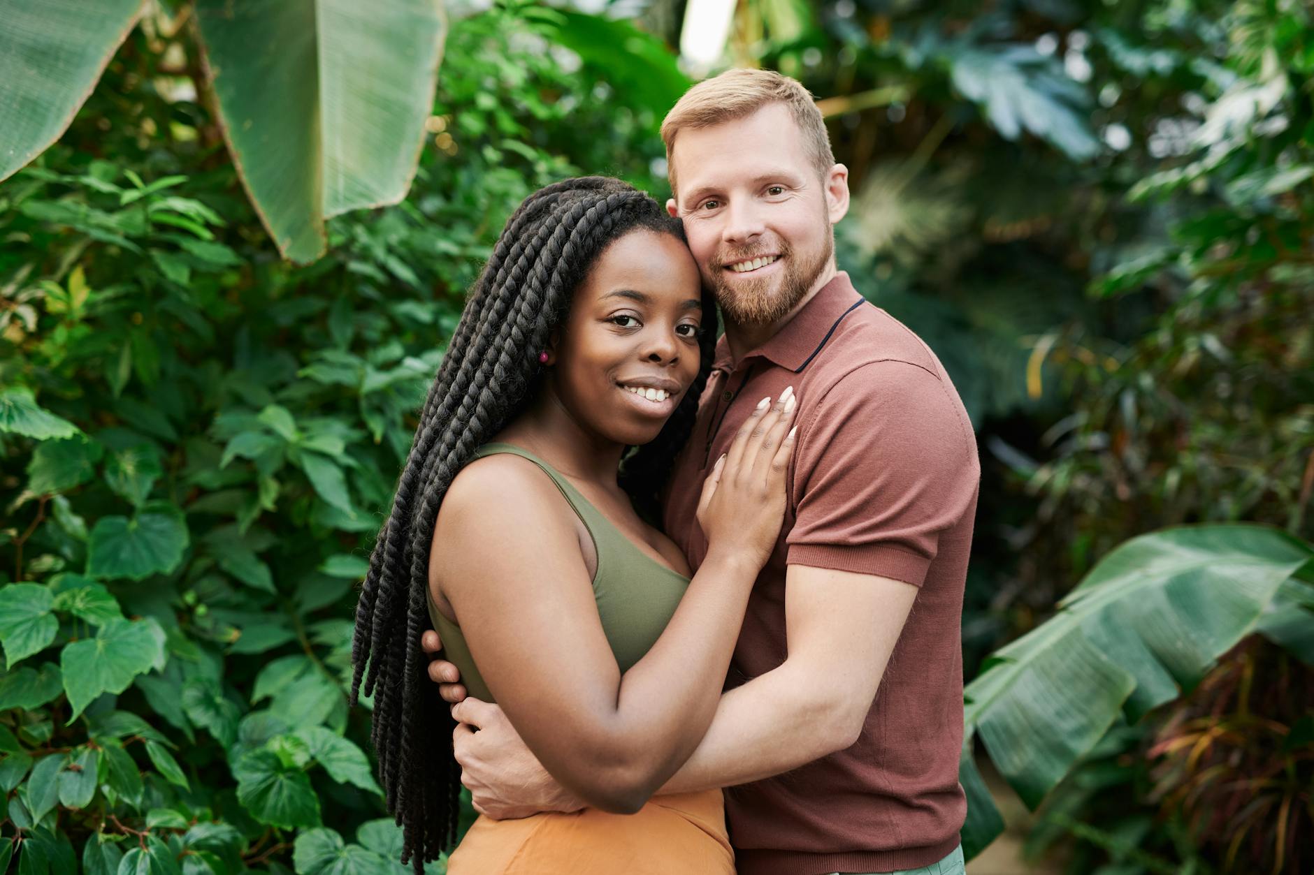 Interracial couple hugging while looking at camera
