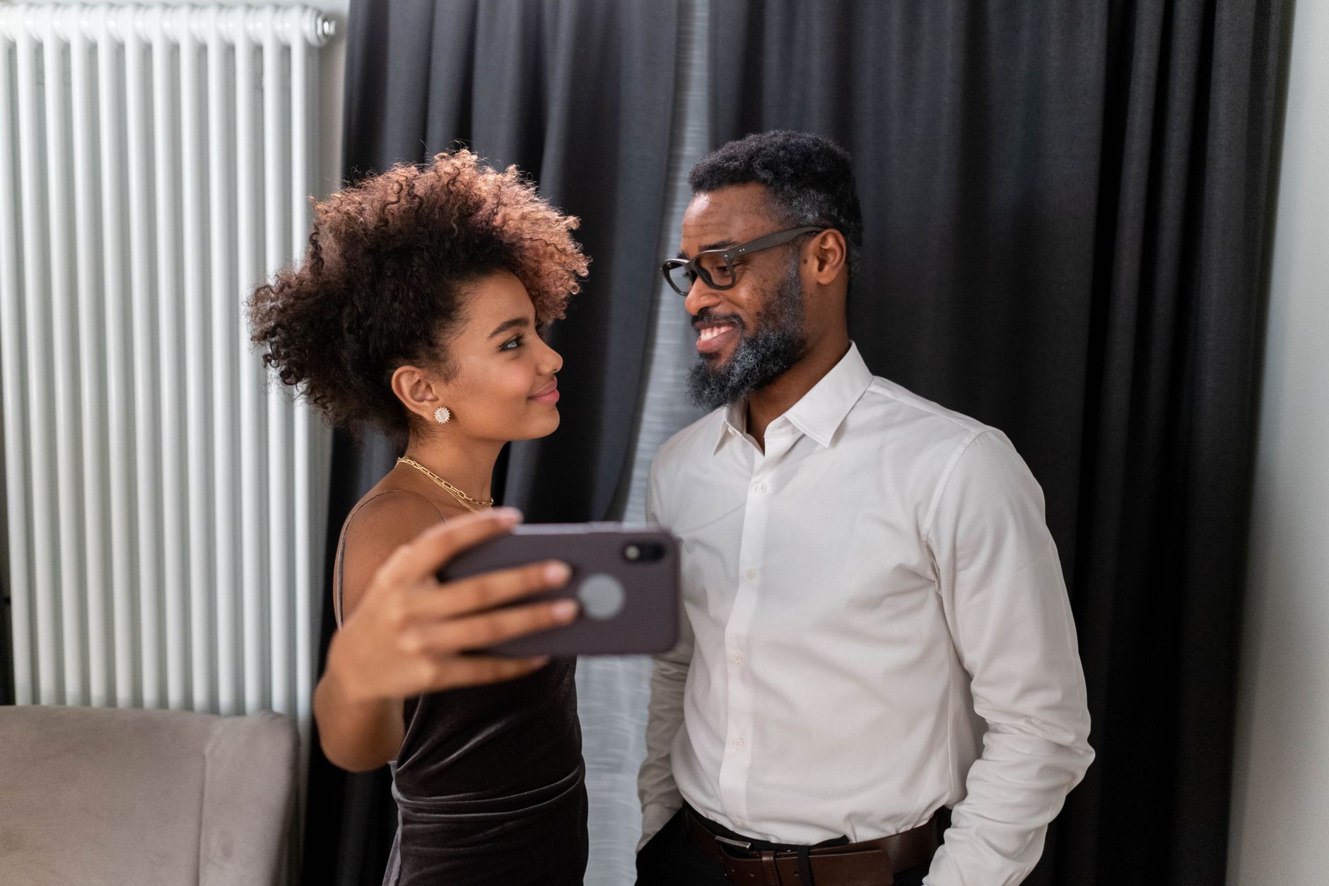 Black couple smiling at each other while woman is holding phone to take a picture