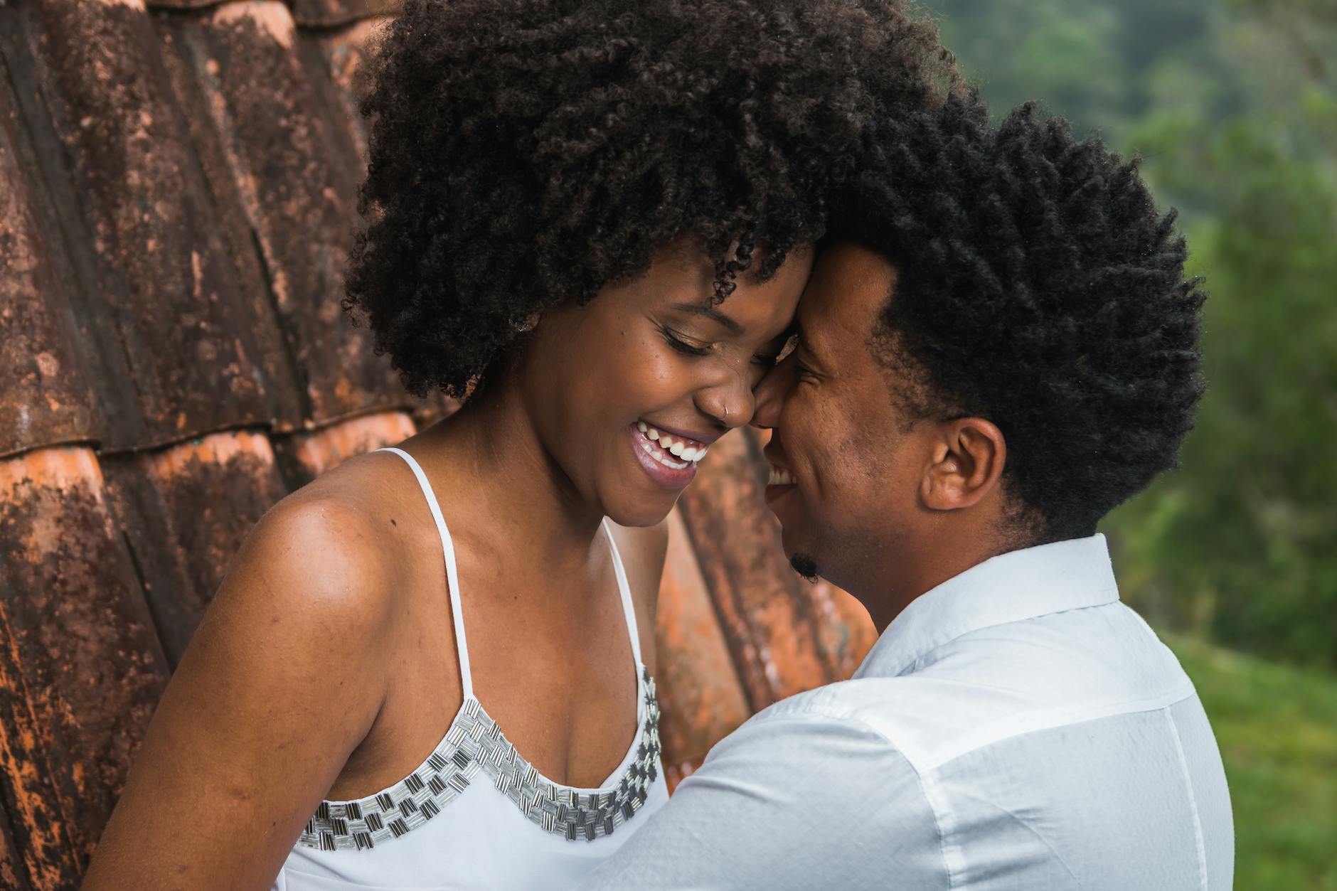 Black couple wearing white smiling and embracing outdoors