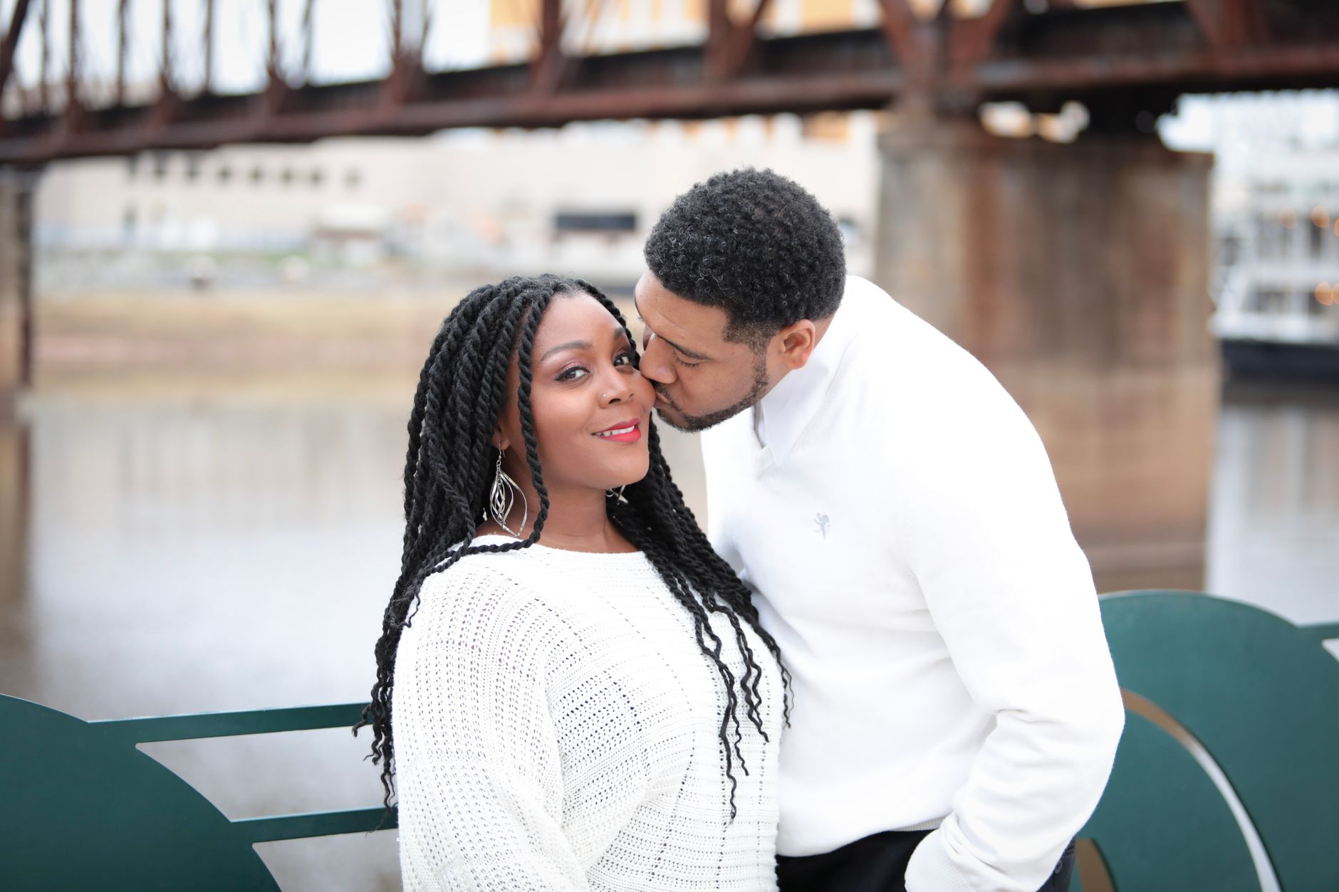 African American couple kissing and smiling by a river bridge